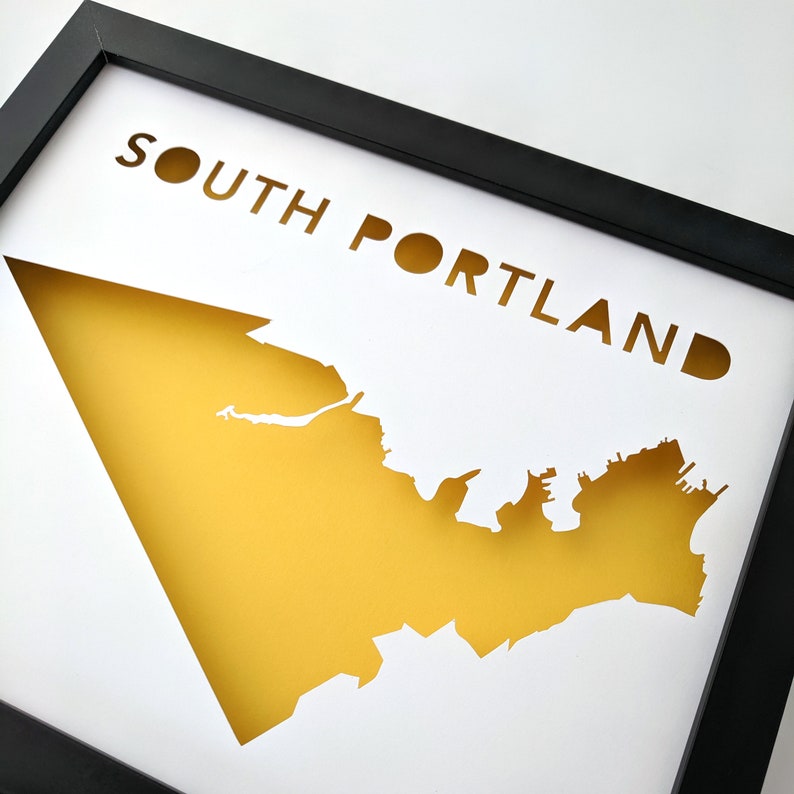 Peut inclure: Une impression encadr&eacute;e blanche avec une silhouette jaune du quartier de South Portland, dans le Maine. Le texte "SOUTH PORTLAND" est d&eacute;coup&eacute; dans le fond blanc.