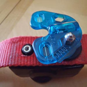 Puede incluir: Un clip de correa para perro de pl&aacute;stico azul con una correa roja unida. El clip tiene un tornillo de metal y un peque&ntilde;o agujero en el centro.