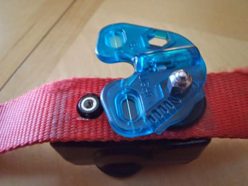 Puede incluir: Un clip de correa para perro de pl&aacute;stico azul con una correa roja unida. El clip tiene un tornillo de metal y un peque&ntilde;o agujero en el centro.