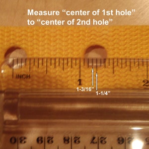 Puede incluir: Una regla amarilla con dos agujeros, midiendo la distancia entre los centros de los agujeros como 1-3/16 pulgadas y 1-1/4 pulgadas.