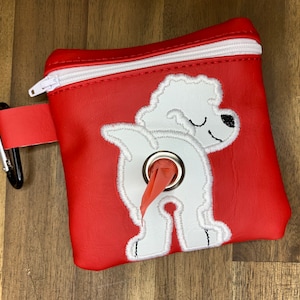 May include: Red zippered pouch with a white embroidered dog design. The dog is white with a red tail and a black nose. The pouch has a black carabiner clip.