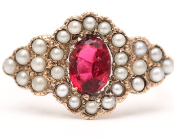 May include: A gold ring with a red gemstone surrounded by a halo of small white pearls.