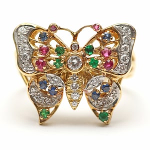 May include: A gold butterfly ring with a large central diamond and smaller diamonds, emeralds, rubies, and sapphires.