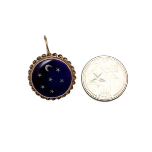 May include: A gold earring with a blue enamel circle featuring a crescent moon and stars. The earring is about the size of a US quarter.