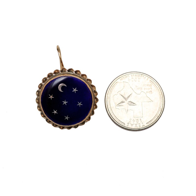 May include: A gold earring with a blue enamel circle featuring a crescent moon and stars. The earring is about the size of a US quarter.