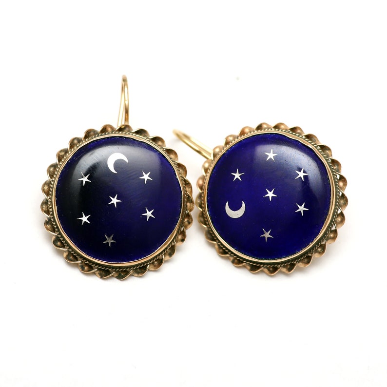May include: A pair of gold earrings with a blue enamel background and white enamel stars and crescent moon design.