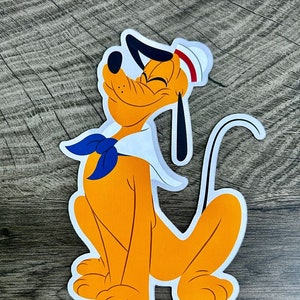May include: A cartoon illustration of a yellow dog wearing a white sailor hat with a red band and a blue neckerchief. The dog is sitting with its tail curled around its body and has a happy expression on its face.