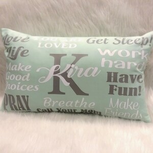 May include: A light green rectangular pillow with white and gray text. The text says "Love Life", "You Are Loved", "Get Sleep", "Work Hard", "Make Good Choices", "Pray", "Breathe", "Call Your Mom", "Make Friends", "Have Fun!" and "Kira".