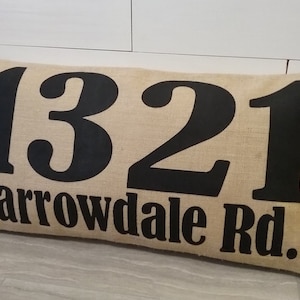 May include: A beige burlap pillow with black lettering that reads "1321 Barrowdale Rd."
