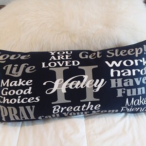 May include: A navy blue pillow with white and silver text. The text reads "Love Life Make Good Choices Pray Breathe Call Your Mom Get Sleep! Work Hard Have Fun Make Friends" with the name "Haley" in the center.