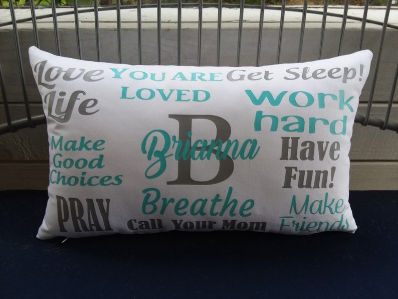 May include: White pillow with gray and teal text. The text says "Love You Are Get Sleep! Life Loved Work Hard Brianna Have Fun! Make Good Choices Pray Breathe Call Your Mom Make Friends".