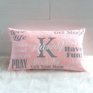 May include: Pink pillow with white text and a gray letter K. The text on the pillow reads "Love Life Make Good Choices Pray Breathe Call Your Mom Make Friends Get Sleep Work Hard Have Fun!" and "Kennedy".