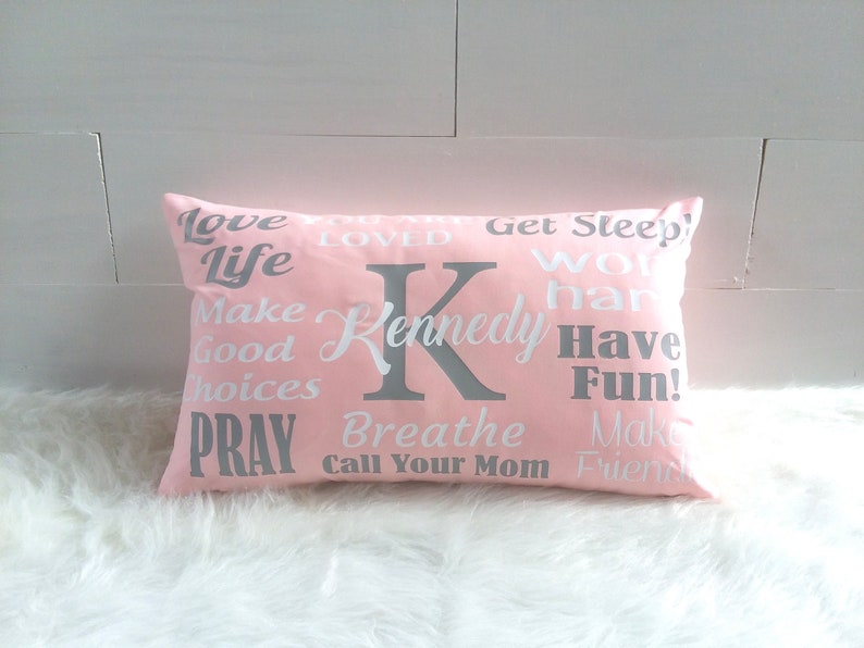May include: Pink pillow with white text and a gray letter K. The text on the pillow reads "Love Life Make Good Choices Pray Breathe Call Your Mom Make Friends Get Sleep Work Hard Have Fun!" and "Kennedy".