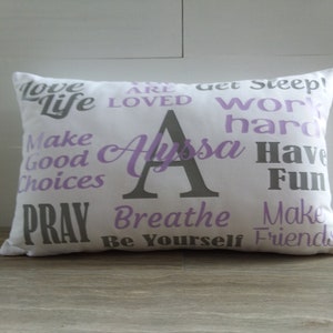 May include: White pillow with purple and gray text. The text says "Love Life", "You Are Loved", "Get Sleep", "Work Hard", "Make Good Choices", "Pray", "Breathe", "Be Yourself", "Make Friends", "Have Fun", and "Alyssa".