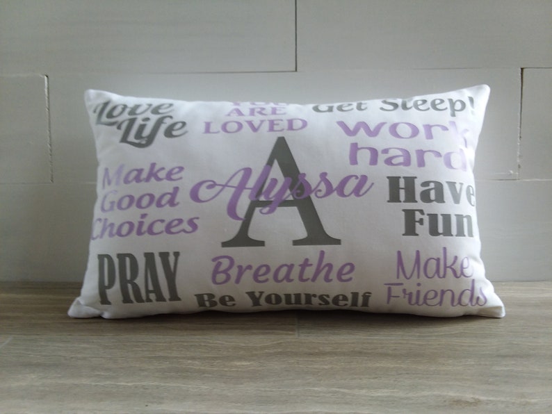 May include: White pillow with purple and gray text. The text says "Love Life", "You Are Loved", "Get Sleep", "Work Hard", "Make Good Choices", "Pray", "Breathe", "Be Yourself", "Make Friends", "Have Fun", and "Alyssa".