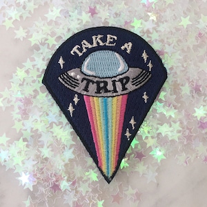Könnte beinhalten: Ein blauer und schwarzer gestickter Aufnäher mit einem UFO und einem Regenbogen. Das UFO trägt den Text "TAKE A TRIP".