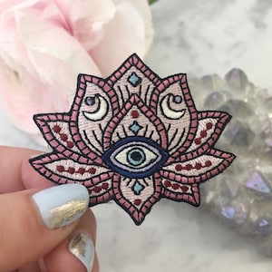 May include: Embroidered pink and blue lotus flower patch with a blue evil eye in the center. The lotus flower has a detailed design with white crescent moons and a geometric pattern.