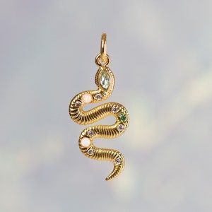 May include: A gold snake charm with green and white gemstones. The snake is coiled and has a textured surface.