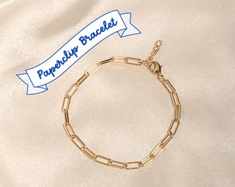 May include: A gold paperclip chain bracelet. The bracelet is made of a series of linked paperclip-shaped metal pieces.