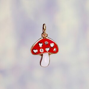 Peut inclure: Un charme en or en forme de champignon rouge et blanc avec des c&oelig;urs blancs et des strass transparents.