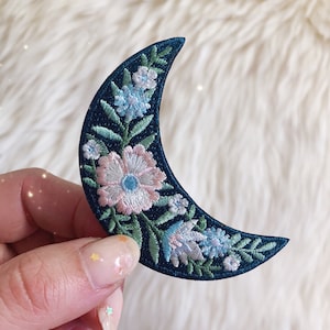 May include: A crescent moon embroidered patch with floral details in shades of pink, blue, and green.