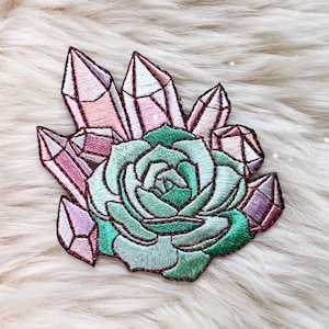 May include: A pink and purple embroidered patch featuring a succulent plant with crystals around it.