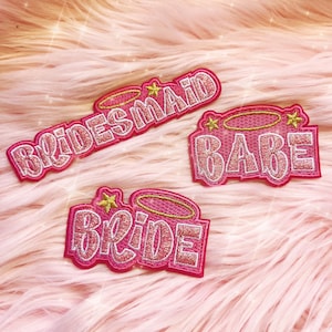 Puede incluir: Tres parches bordados en rosa y blanco con detalles dorados. Los parches dicen "Bride", "Bridesmaid" y "Babe".