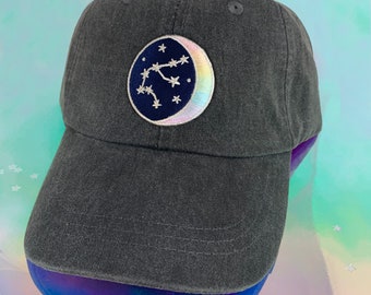 May include: A black baseball cap with an embroidered patch of a crescent moon and stars. The moon is iridescent and the stars are white.