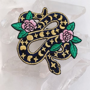 May include: Embroidered iron-on patch featuring a black snake with gold crescent moons and stars, surrounded by pink roses and green leaves.