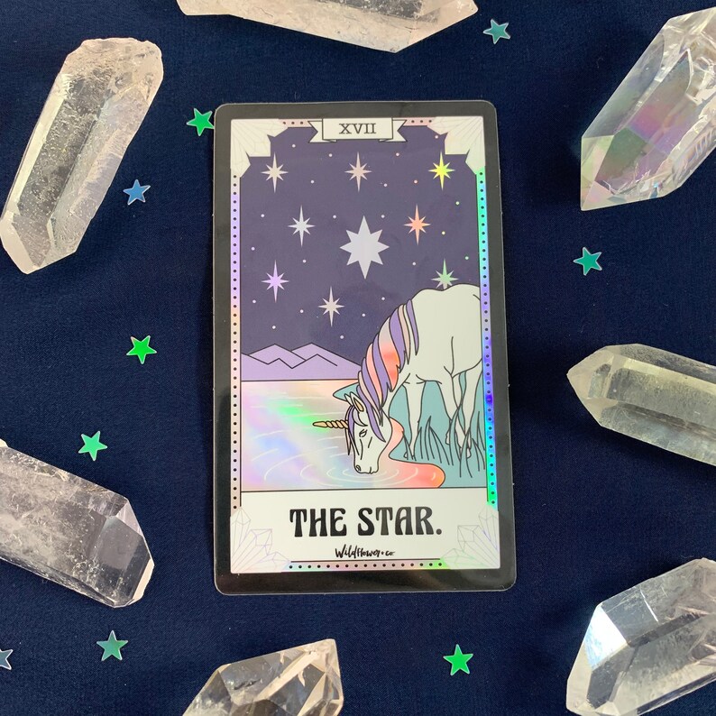 May include: A holographic tarot card with a purple and white unicorn drinking from a lake under a starry night sky. The card is labeled "The Star" and "XVII".