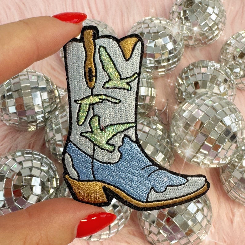Puede incluir: Un parche bordado de bota vaquera azul y blanca con costuras doradas y p&aacute;jaros verdes. El parche est&aacute; sobre un fondo rosa peludo con bolas de discoteca plateadas.