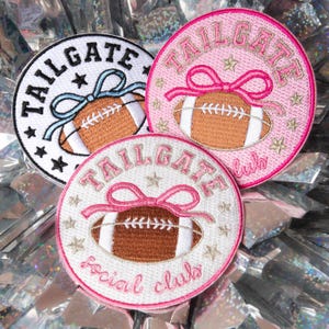 May include: Three embroidered patches with football and text designs. One is white with black trim and the word "TAILGATE" in black. Another is pink with a pink bow and the words "TAILGATE club". The third is white with pink trim and the words "TAILGATE social club".