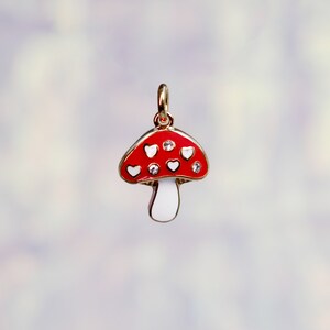 Peut inclure: Un charme en forme de champignon rouge et blanc avec des accents en forme de c&oelig;ur blanc et des strass transparents. Le charme est en m&eacute;tal et a une finition dor&eacute;e.