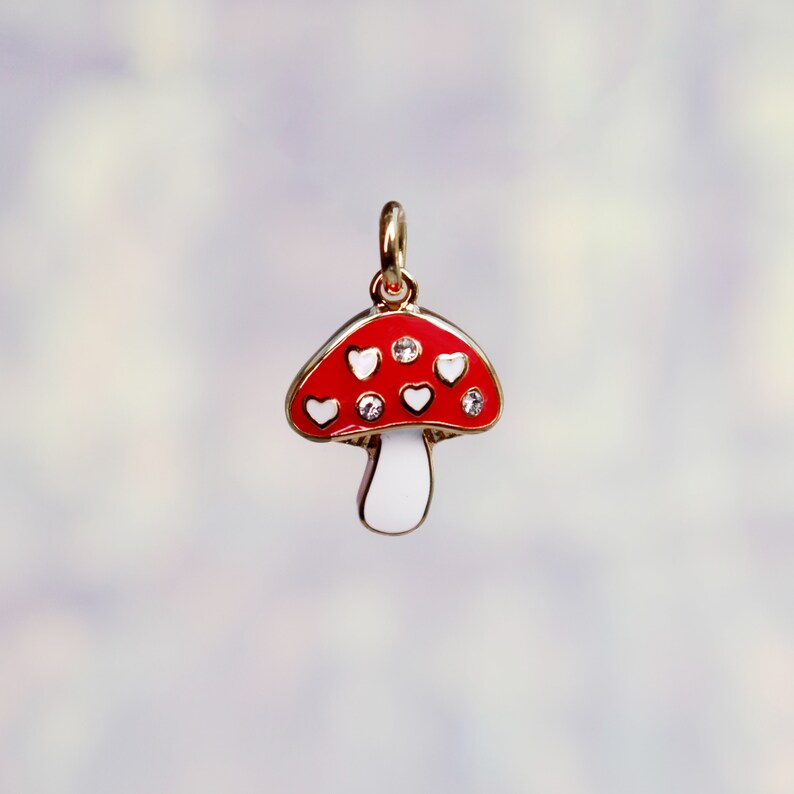 Peut inclure: Un charme en forme de champignon rouge et blanc avec des accents en forme de c&oelig;ur blanc et des strass transparents. Le charme est en m&eacute;tal et a une finition dor&eacute;e.