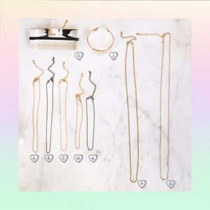 May include: A set of nine gold and black chain necklaces on a white marble background. The necklaces are labeled with letters A through Q.