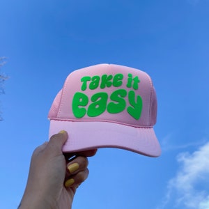 May include: Pink trucker hat with a green "Take it easy" slogan in a retro font.