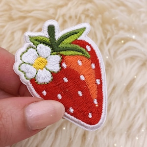 May include: Embroidered iron-on patch of a red strawberry with white seeds and a white flower with a yellow center.
