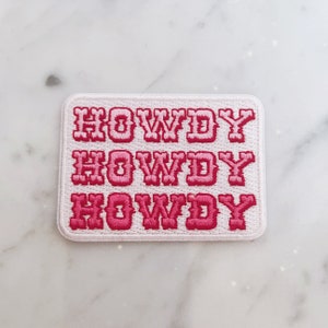 May include: A white patch with pink embroidered text that reads "HOWDY HOWDY HOWDY".