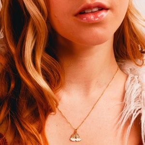 May include: A gold chain necklace with a small rainbow pendant. The pendant has a sparkly design and is made of metal.