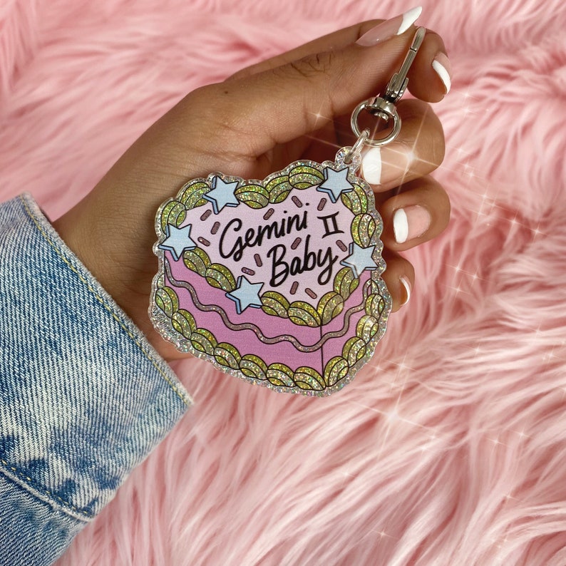 May include: A pink and green glitter heart-shaped keychain with the text "Gemini II Baby" and white stars.