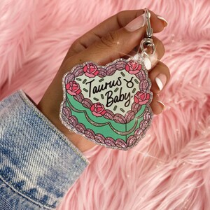 May include: A sparkly green and pink heart-shaped keychain with the text "Taurus ♉ Baby" and a pink rose design.