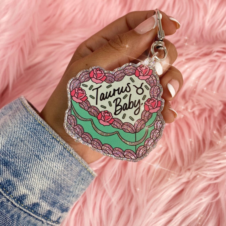 May include: A sparkly green and pink heart-shaped keychain with the text "Taurus ♉ Baby" and a pink rose design.