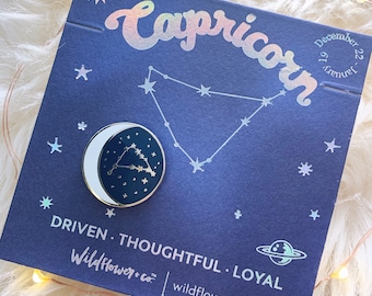 May include: A circular enamel pin featuring a white crescent moon and a dark blue sky with a gold constellation, attached to a dark blue card printed with the word Capricorn, the dates December 22-January 19, and the text DRIVEN, THOUGHTFUL, LOYAL.