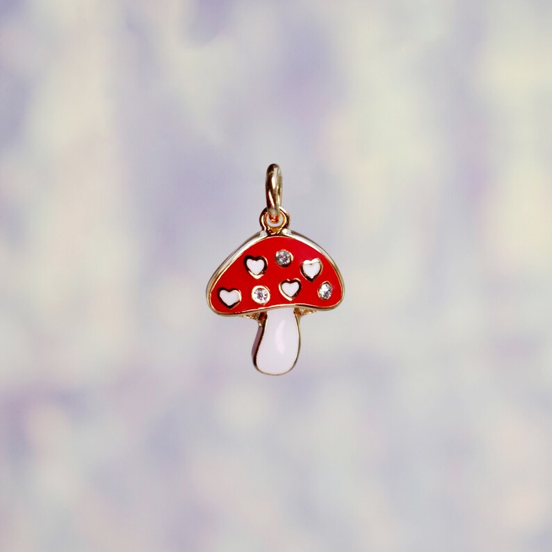 Peut inclure: Un charme en or en forme de champignon rouge et blanc avec des c&oelig;urs blancs et des strass transparents.