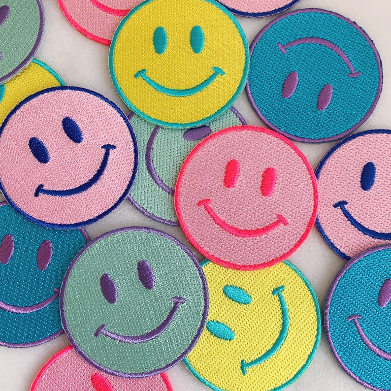 Puede incluir: Surtido de parches bordados con caritas sonrientes de colores. Los parches est&aacute;n hechos de fieltro y tienen fondos y caras sonrientes de diferentes colores.