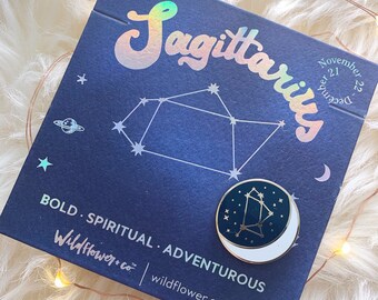 May include: A blue and gold Sagittarius constellation pin with a white background. The pin is on a blue card with the words "Sagittarius" and "November 21 - December 22" in white text. The card also has the words "Bold. Spiritual. Adventurous" and "Wildflower.co" in white text.