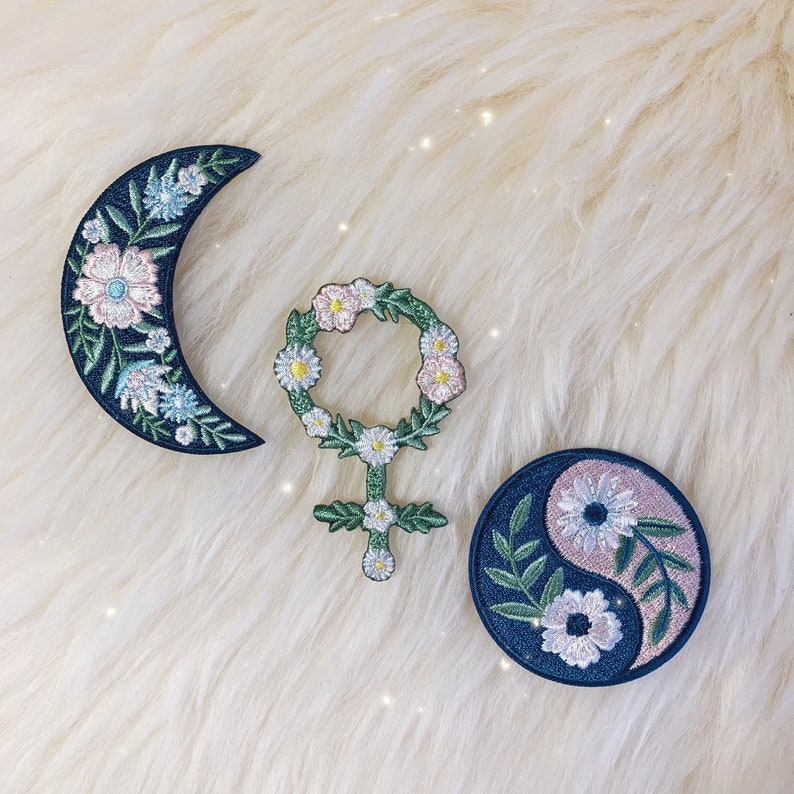 May include: Three embroidered iron-on patches with floral designs. The patches are a crescent moon, a yin-yang symbol, and a female symbol with a flower crown.