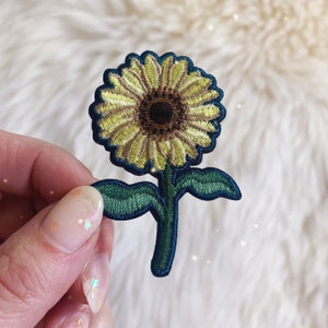 May include: A yellow and green embroidered sunflower patch with a brown center.
