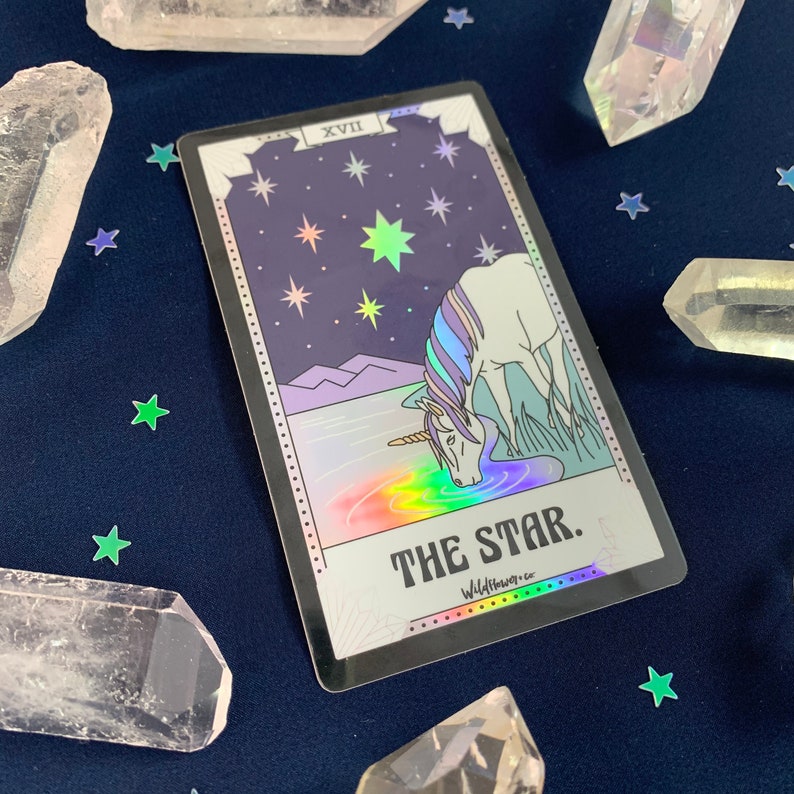 May include: A holographic tarot card with a black border. The card depicts a unicorn drinking from a pool of water with a rainbow reflection. The card is labeled "The Star" and "WildUnknown."