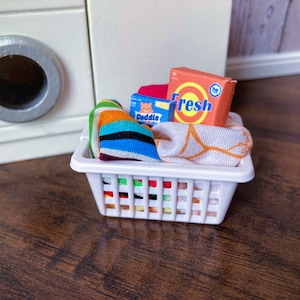 May include: A white laundry basket filled with colorful striped towels, a box of laundry detergent that says "Fresh", and a box of laundry detergent that says "Cuddle".